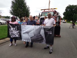 Lift Every Voice marching in a local parade with banner.